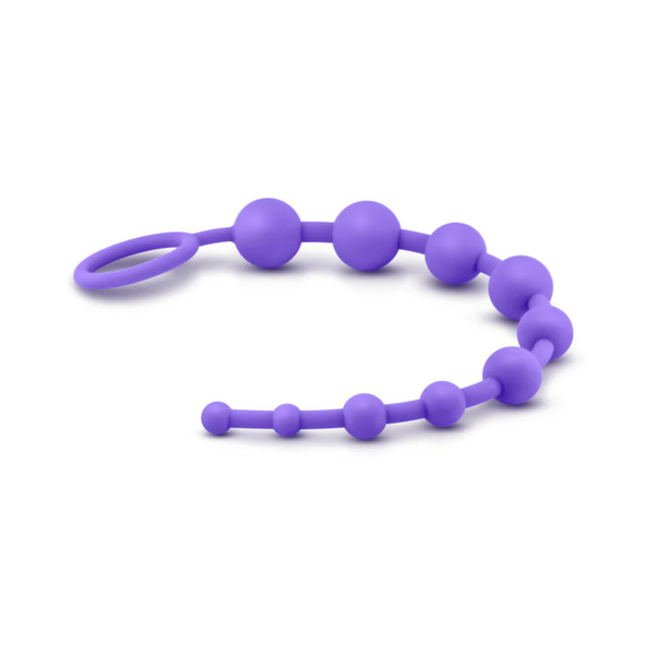 Side view of the purple silicone bead strand lying horizontally across a plain white surface. The flexible strand gently curves, showing the gradual increase in bead size from tip to ring.
