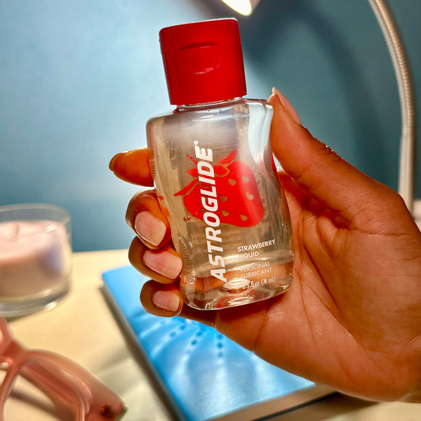 A person's hand holding a bottle of Astroglide Strawberry Liquid Personal Lubricant.