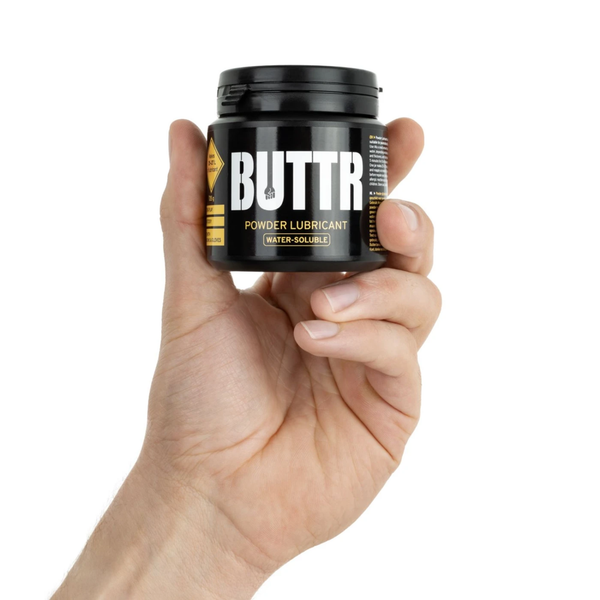 Scale reference photo showing a hand holding the 135 g black tub of BUTTR Powder Lubricant.