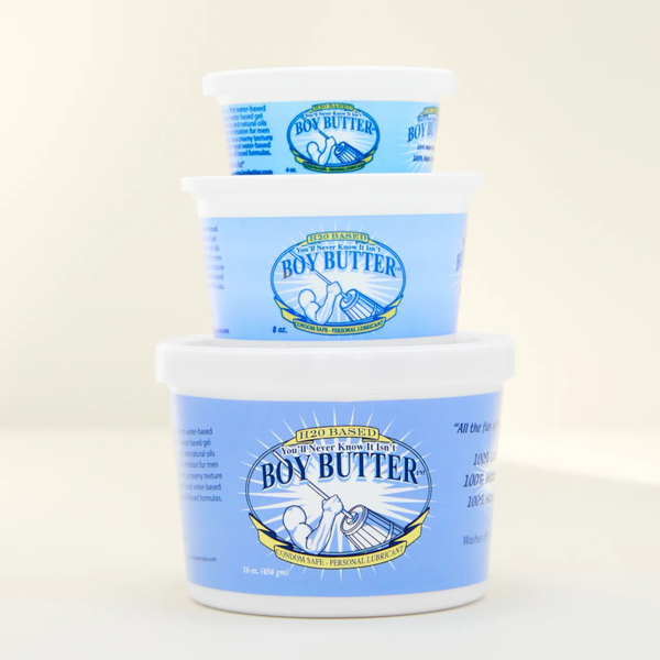 A shot showing a stack of three white plastic tubs of Boy Butter H2O Based Personal Lubricant against a light cream background, stacked largest on the bottom to smallest on top. All have the blue label and are marked "H2O BASED" and "CONDOM SAFE PERSONAL LUBRICANT."
