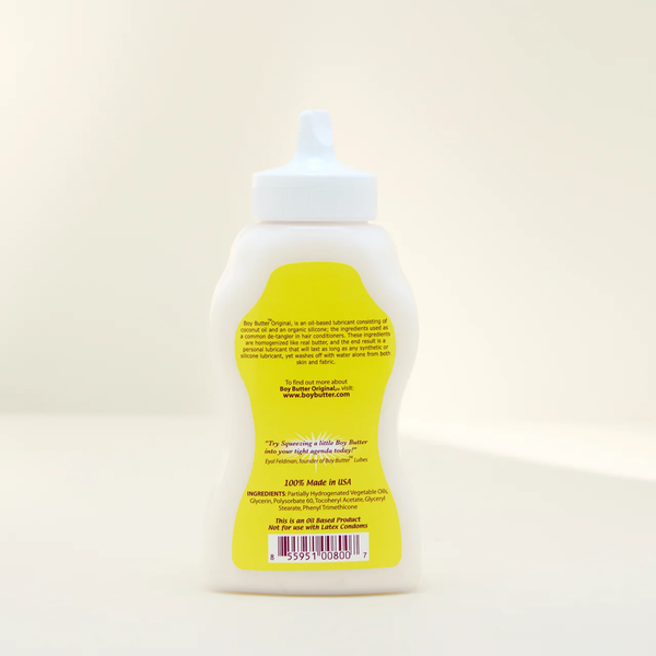 A shot showing the back label of the Boy Butter Original Personal Lubricant in a white, contoured, squeeze bottle with a white nozzle. The yellow label details the product's oil-based composition, its uses, and a warning that it is Not for use with Latex Condoms.