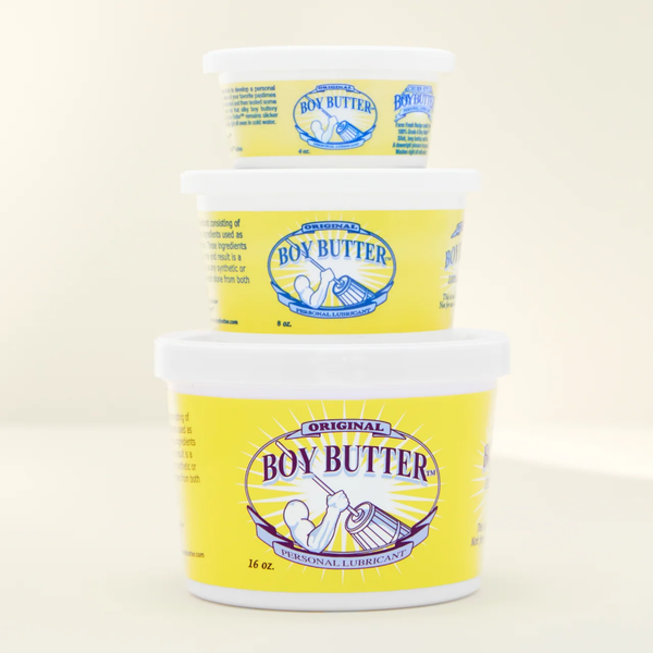 A shot showing a stack of three white plastic tubs of Boy Butter Original Personal Lubricant against a light cream-colored background. The tubs are stacked largest (16 oz.) on the bottom, medium (8 oz.) in the middle, and smallest (2 oz.) on top, each featuring the yellow label with the image of a person churning butter.