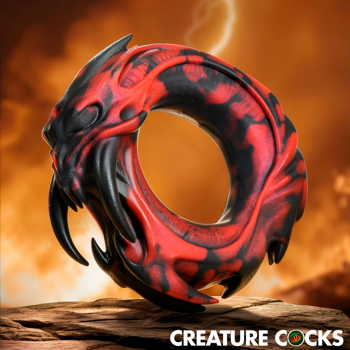 Studio product shot of the red and black marble-patterned silicone cock ring with molded fang and claw details resting on a stone ledge.