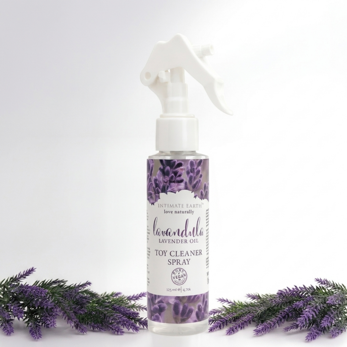 Nature-inspired studio shot of the Intimate Earth Lavandula lavender oil toy cleaner spray bottle flanked by artificial lavender sprigs.