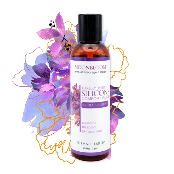 Artistic product display showing the 120 ml (4 fl oz) bottle of Intimate Earth Moon Bloom silicone comfort glide centered over a purple and gold watercolor floral backdrop.