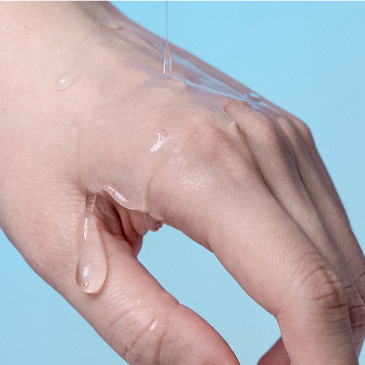 Close-up macro photo showing clear lubricant jelly dripping smoothly over a hand against a light blue background.