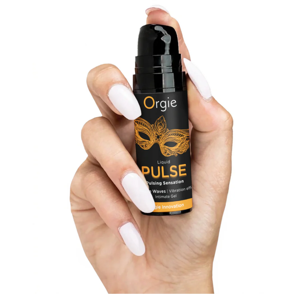 A hand with long white manicured nails holds the 15ml bottle of Orgie Liquid Pulse. The cap is removed to show a black pump dispenser. The small size of the bottle emphasizes its portability and ease of use.