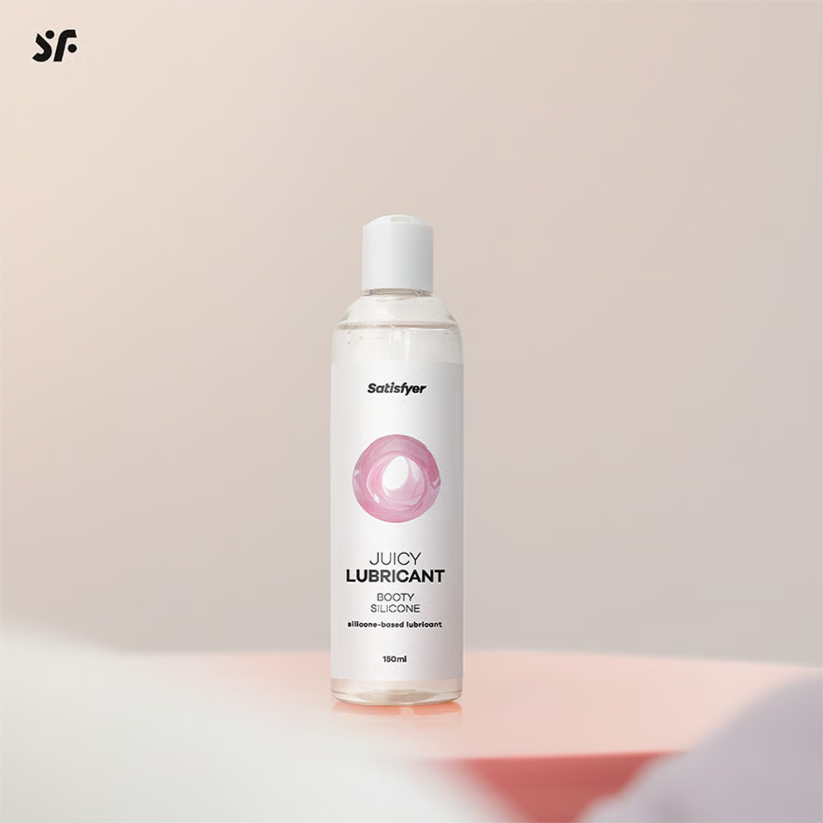 Studio product shot of the 150 ml Satisfyer Booty Silicone Lubricant bottle standing upright on a pink pedestal surface against a soft-focus background.