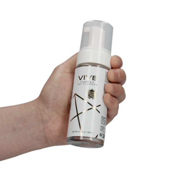 Hand-held product shot showing a hand holding the 140 ml (4.7 fl oz) bottle of Shots Vive Foaming Toy Cleaner.
