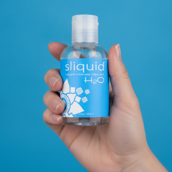 Straight-on shot of a hand holding the clear bottle of Sliquid H2O natural intimate lubricant with its blue flower-graphic label.