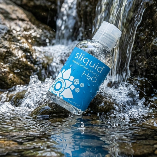 Nature-inspired product shot of the Sliquid H2O water-based lubricant bottle resting among rocks in a fresh, flowing freshwater stream.
