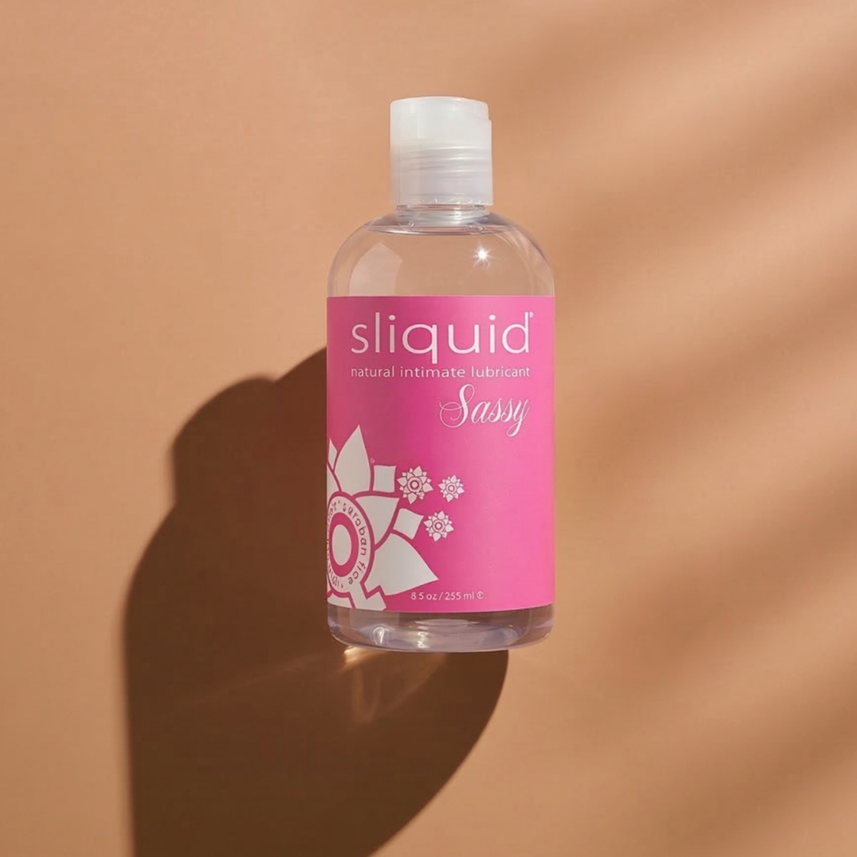 Direct front view of the clear 8.5 oz (255 ml) Sliquid Sassy bottle centered under warm, dramatic lighting and shadows.