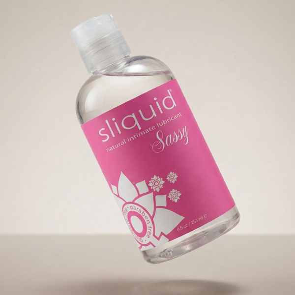 Floating perspective shot of the Sliquid Sassy natural intimate lubricant bottle angled over a light surface with a soft shadow below.