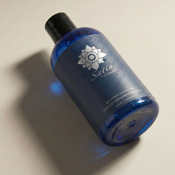 Upright studio product view of the cobalt blue 8.5 oz (255 ml) bottle of Sliquid Satin natural intimate moisturizer covered in fine water condensation, featuring a dark blue label and black cap.