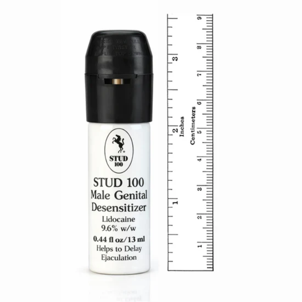 A white STUD 100 spray bottle placed next to a ruler for scale. The bottle stands approximately 3 inches (7.5 cm) tall, emphasizing its discreet and portable size.