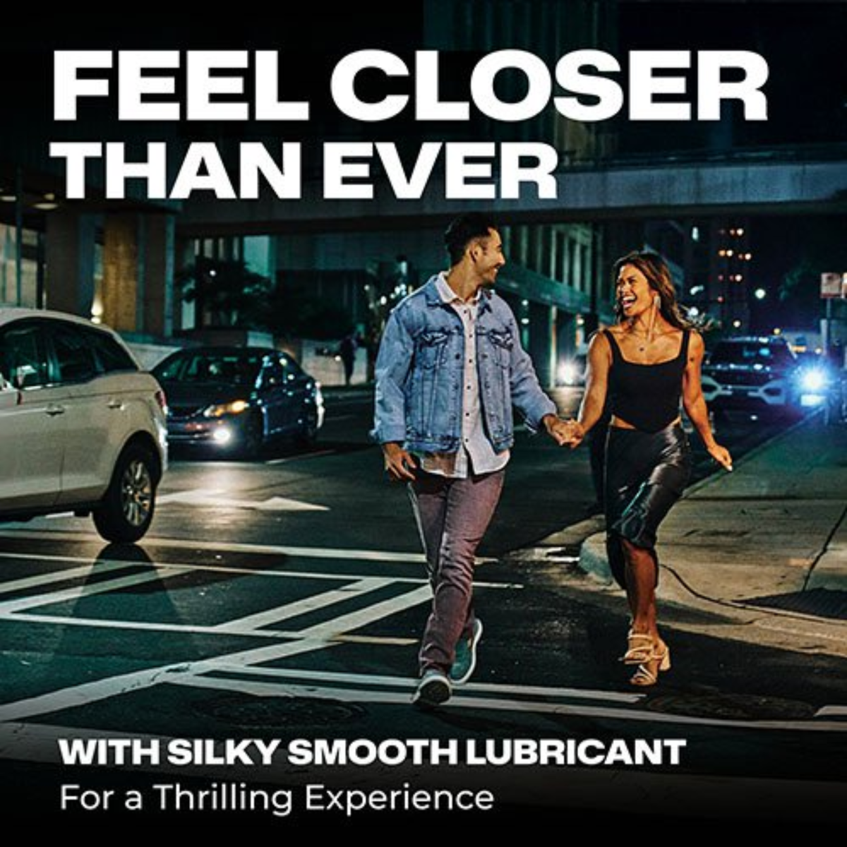 A lifestyle photograph showing a smiling young couple walking hand-in-hand down a city street at night. The man is wearing a denim jacket and maroon pants, while the woman is wearing a black tank top, a black leather skirt, and high heels. Overlaying the top of the image is the large text "FEEL CLOSER THAN EVER," and the bottom reads "WITH SILKY SMOOTH LUBRICANT For a Thrilling Experience."