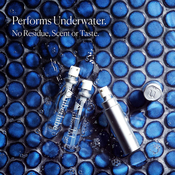 Two clear "uberlube" bottles and one silver pump bottle are submerged in water with blue circular tiles. The text highlights that the product "Performs Underwater. No Residue, Scent or Taste," suggesting its use as a personal lubricant available from Worldcondoms.