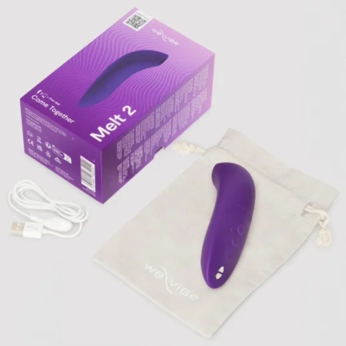 Product set photo displaying the purple We-Vibe Melt 2 massager resting on a light beige drawstring storage pouch next to its retail box and magnetic USB charging cable.