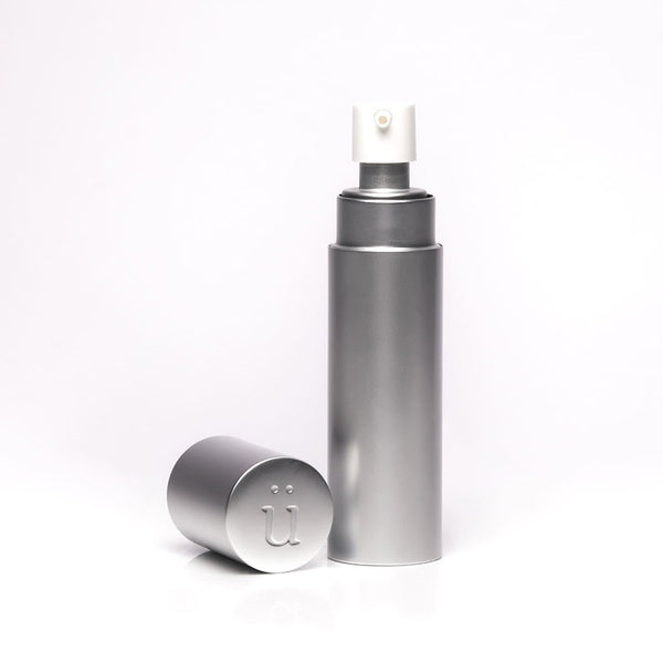 A tall, slender silver refillable case stands next to a clear glass bottle of "überlube" with a white pump top, both items for personal lubricant available at Worldcondoms.